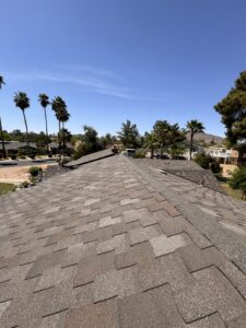 A professionally installed asphalt shingle roof by a reliable roofing contractor in Arizona, set under a clear blue sky with palm trees and houses in the background.